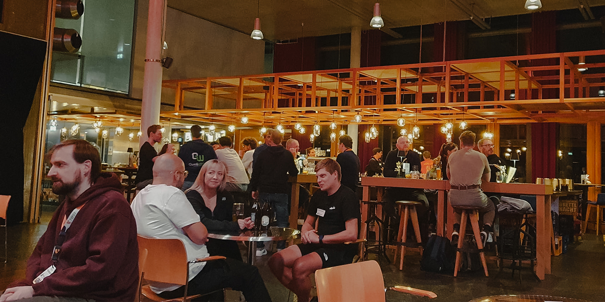 Eine Gruppe von Menschen sitzt an einem Tisch in einer Bar, während andere an der Theke Getränke bestellen.